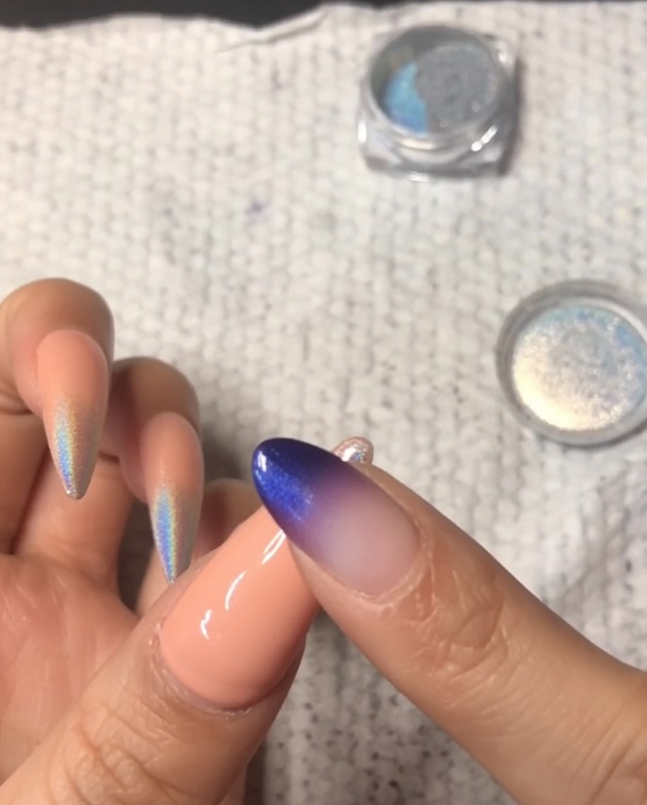 Un primo piano di un dito che strofina della polvere cromata olografica sulla punta di un mignolo, creando una sfumatura ombré.