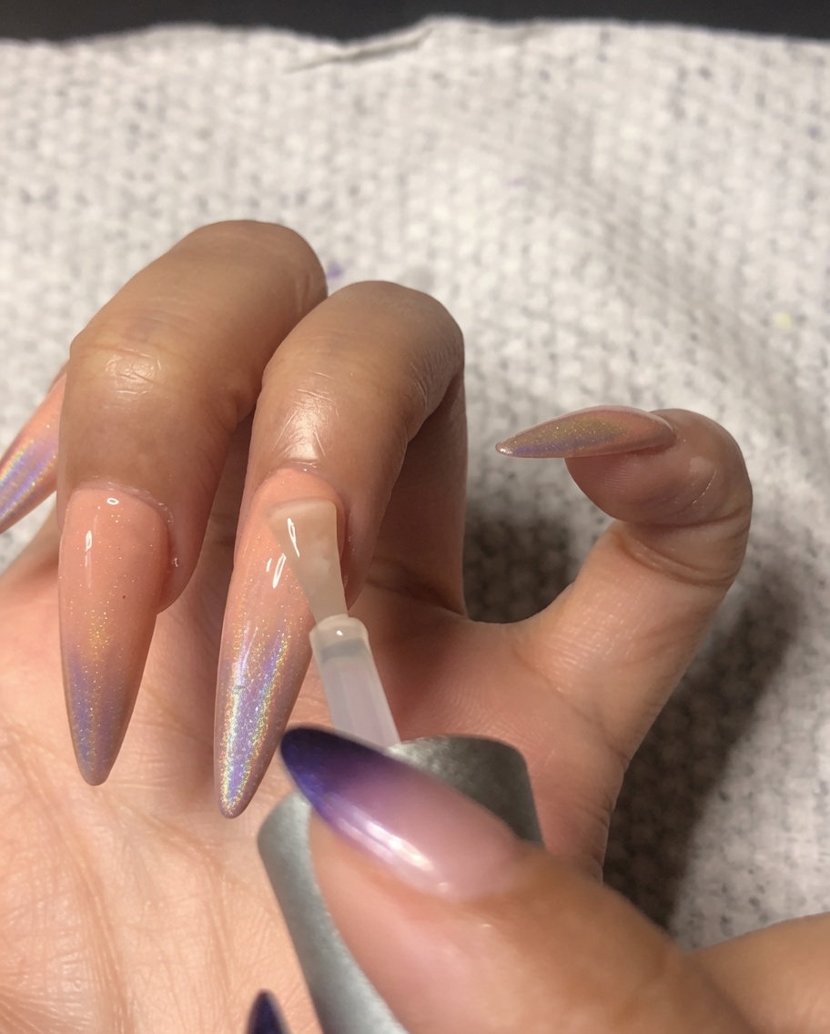 Un pennello per unghie che applica un top coat ultra-lucido sullanulare, sigillando la nail art ombré olografica.