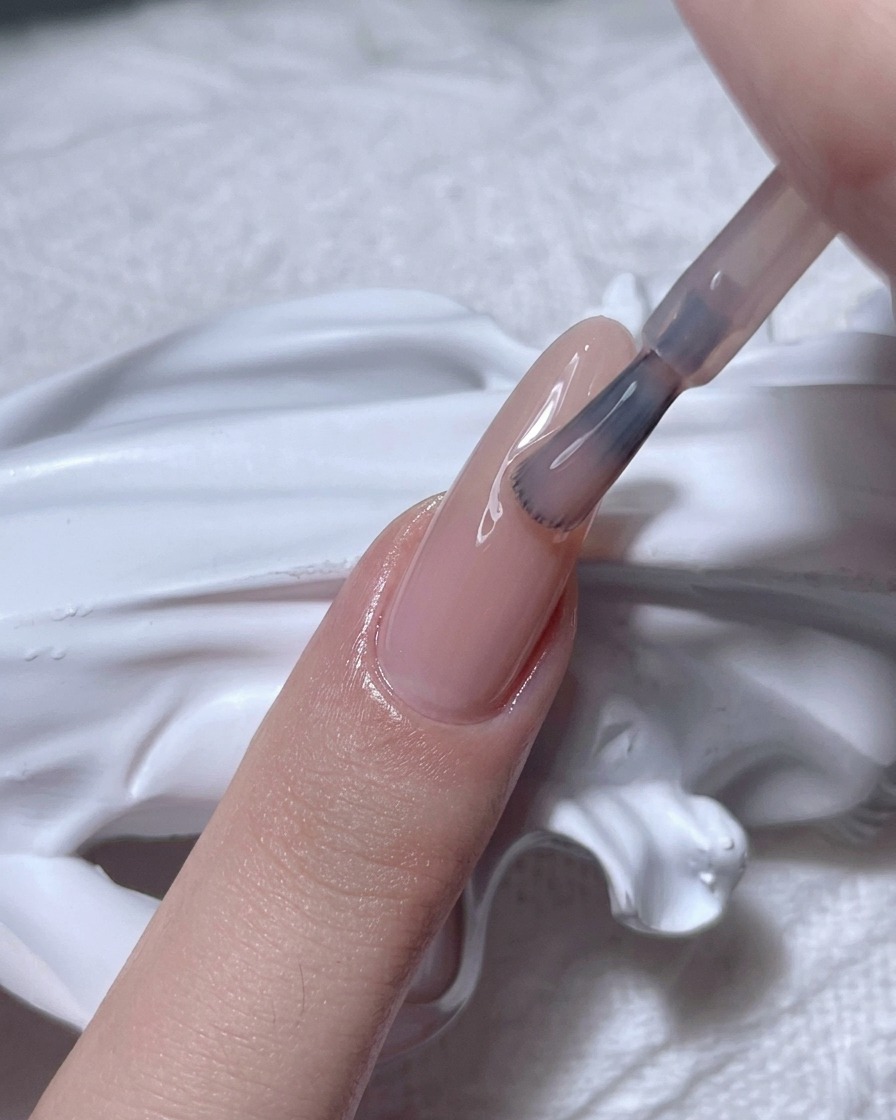 Un pennello applica uno smalto gel nude semi-trasparente su ununghia naturale.