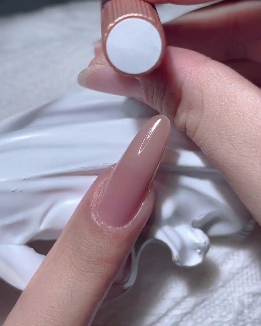 Una mano tiene un flacone di smalto gel nude.
