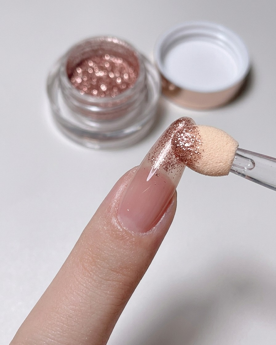 Un applicatore in spugna strofina la polvere oro rosa sulla punta di ununghia nude.