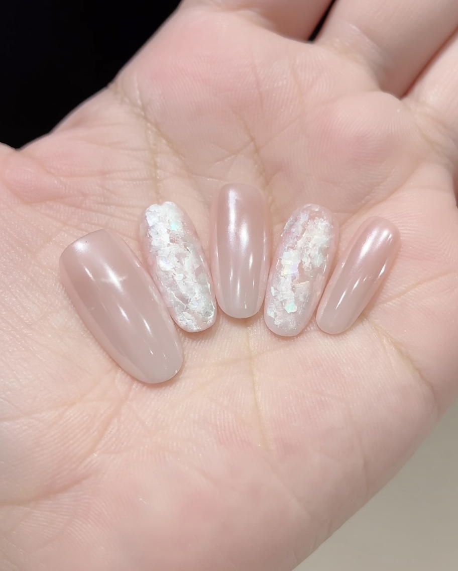 Pinzette che posizionano scaglie di conchiglia iridescenti su ununghia rivestita di gel.