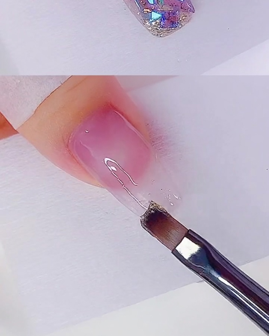 Un pennello piatto applica uno strato sottile di gel glitter oro rosa sulla punta dellunghia.