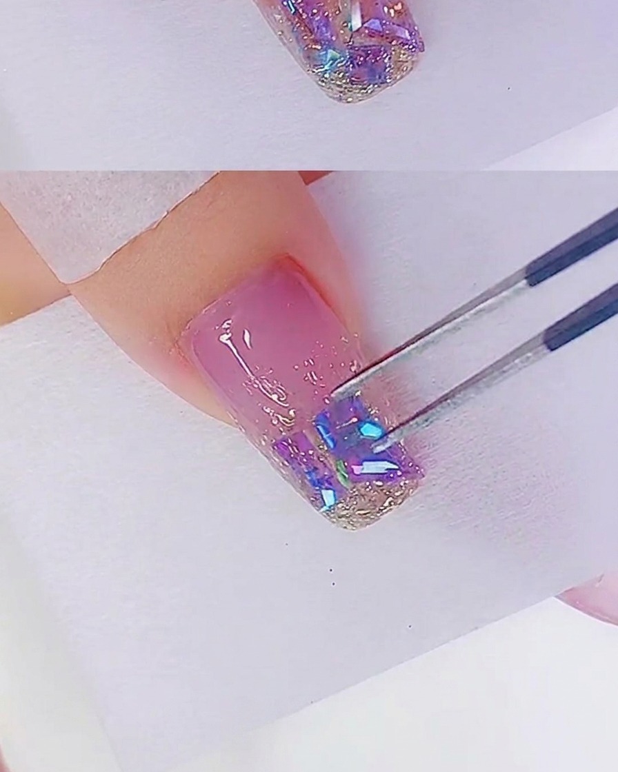 Primo piano di una pinzetta che sistema gli strass sullunghia decorata con gel glitter oro rosa.
