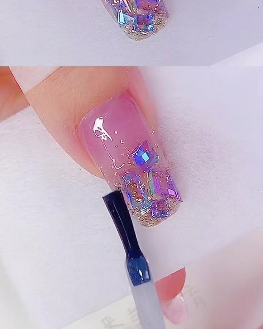 Un pennello applica un top coat trasparente su ununghia decorata con glitter e strass.