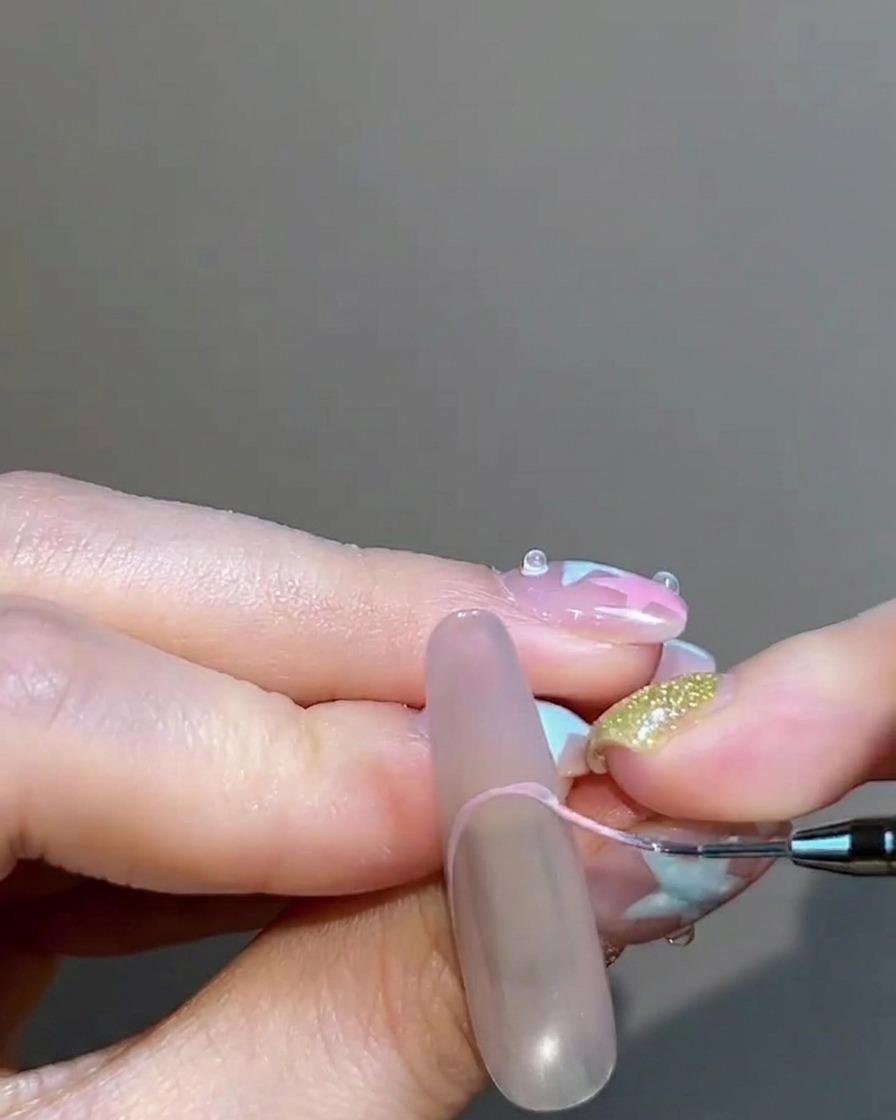 Un pennello liner sottile che dipinge un French tip color rosa nude sullunghia.
