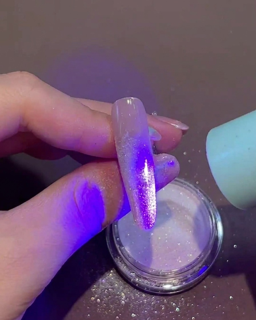 Una mano che tiene una lampada UV/LED portatile sopra lunghia con polvere glitterata sulla punta.