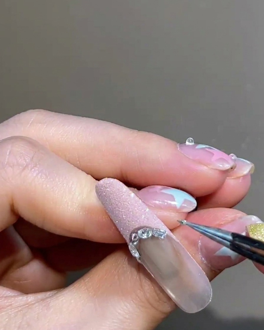 Dettaglio di pinzette che posizionano una piccola borchia argentata sul bordo del French tip.