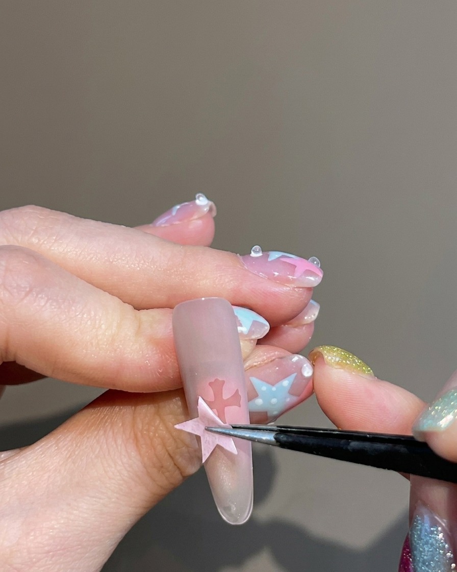Pinzette che rimuovono lo sticker, lasciando una silhouette a forma di croce sullunghia blush.