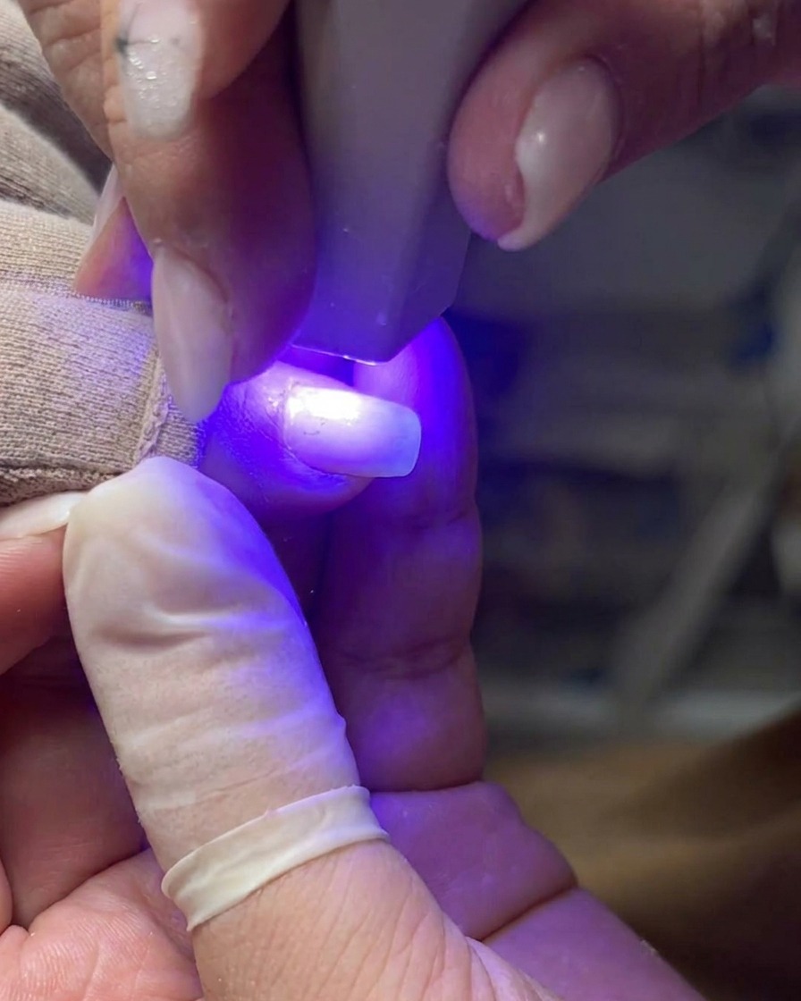 Un pennello professionale applica uno strato uniforme di gel base trasparente sullunghia.