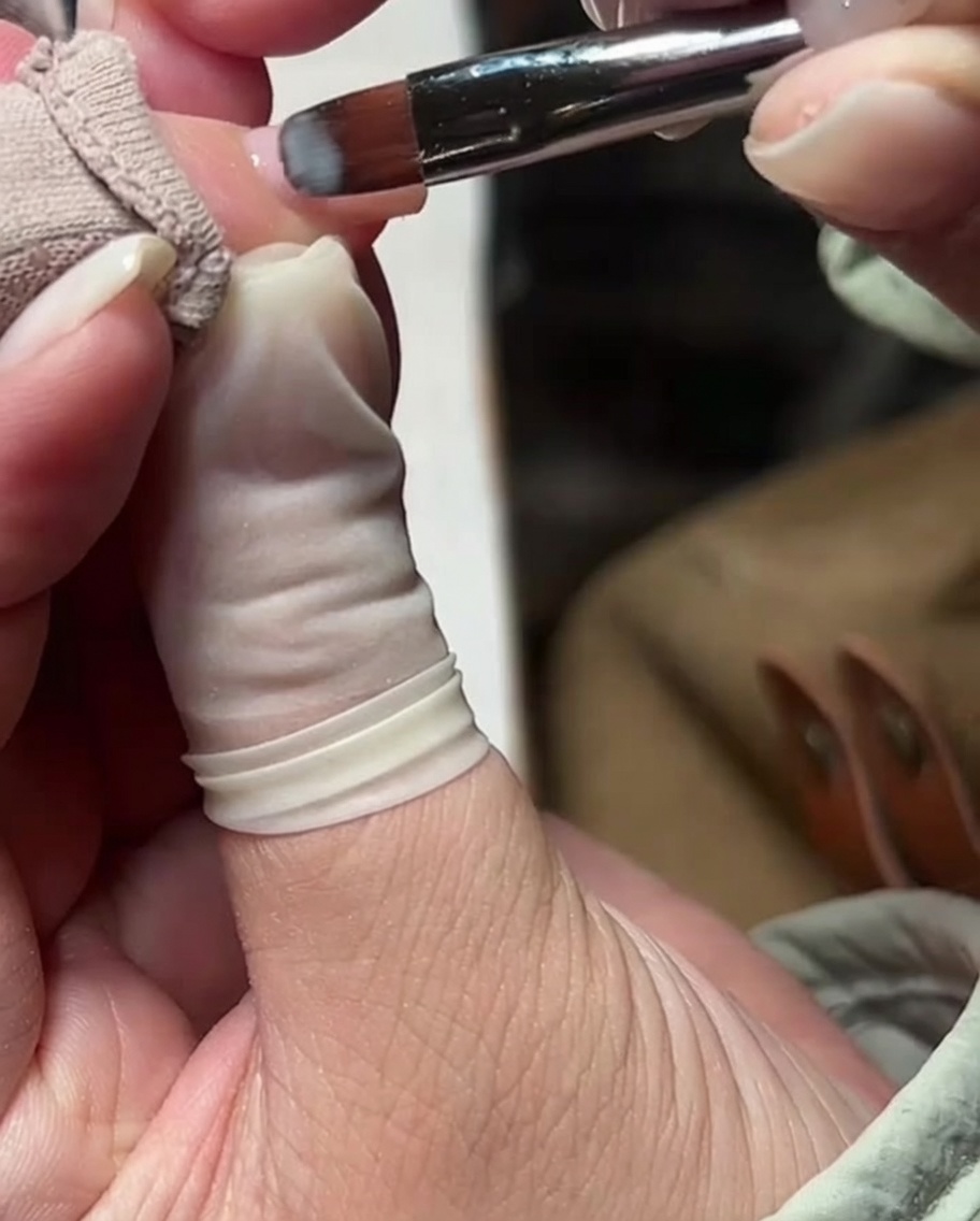 Un pennello da gel applica uno strato sottile di smalto gel nude milky sullunghia.