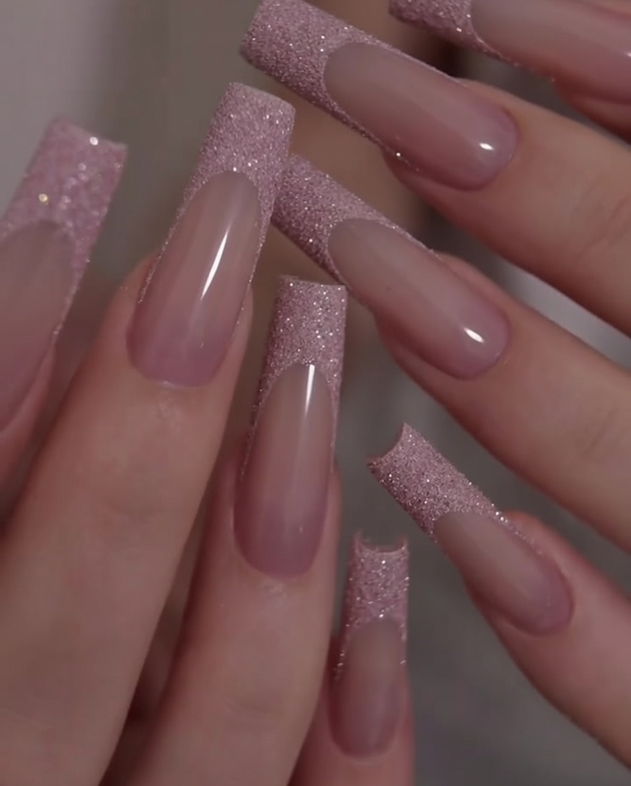 Uno scatto ravvicinato delle mani ruotate per mostrare il contrasto tra la base rosa e le punte French glitterate.