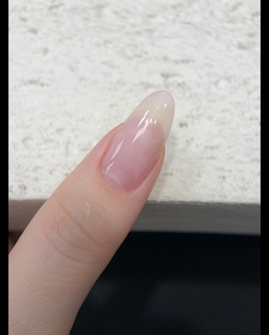 Un pennello che applica uno smalto gel jelly traslucido rosa nude su ununghia naturale.