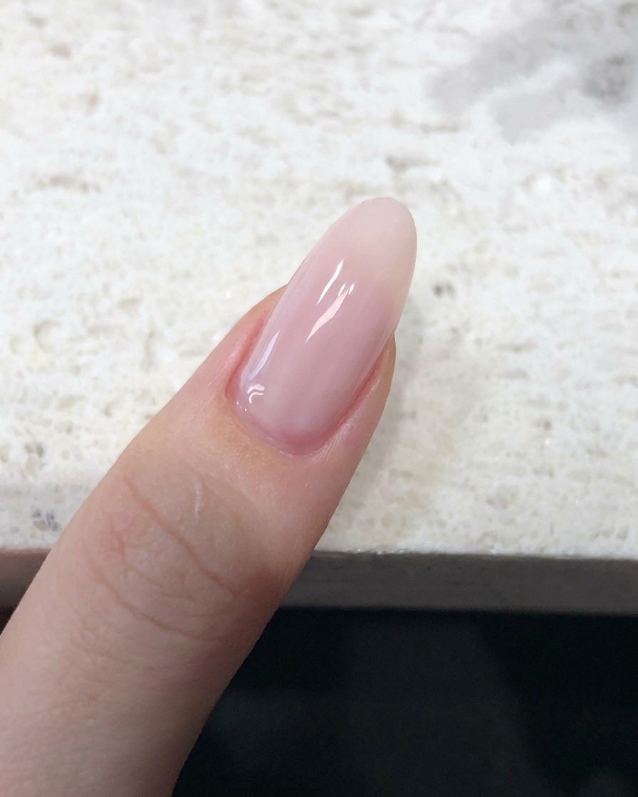 Primo piano di ununghia ricoperta da uno smalto jelly rosa nude trasparente con una finitura liscia.