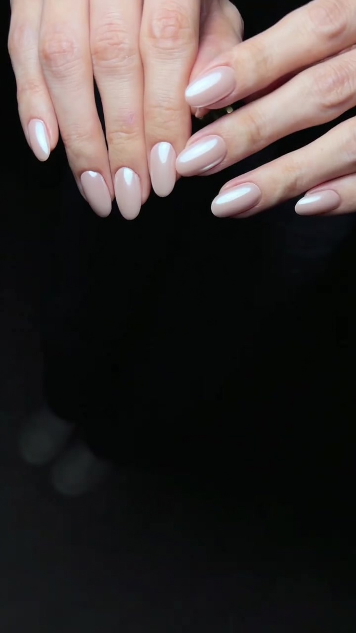 Primo piano di eleganti unghie a mandorla caratterizzate da una base in gel rosa tenue e una finitura cromata color perla.