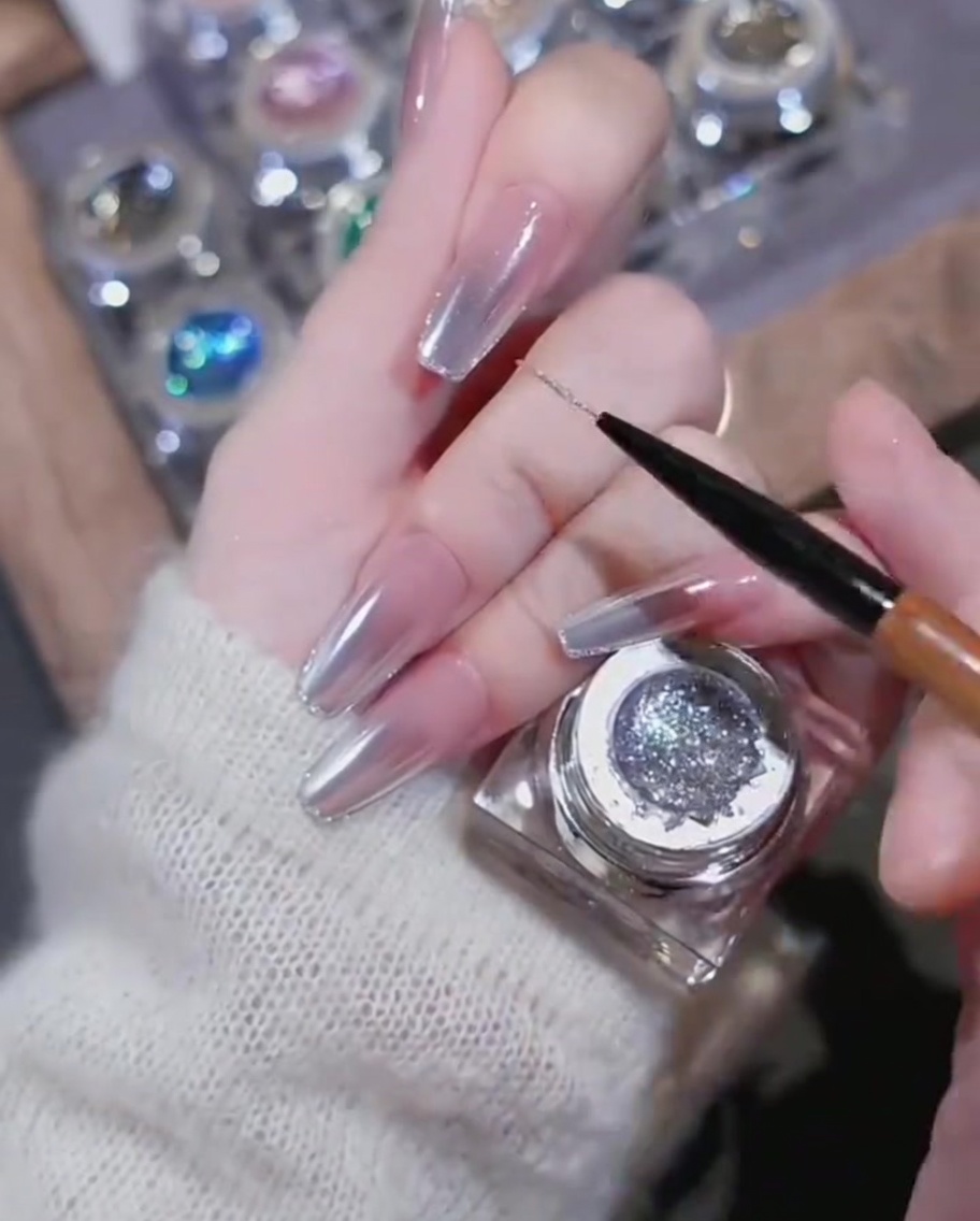 Primo piano di un ciondolo in strass a forma di cuore applicato su ununghia decorata con linee in gel lucido.