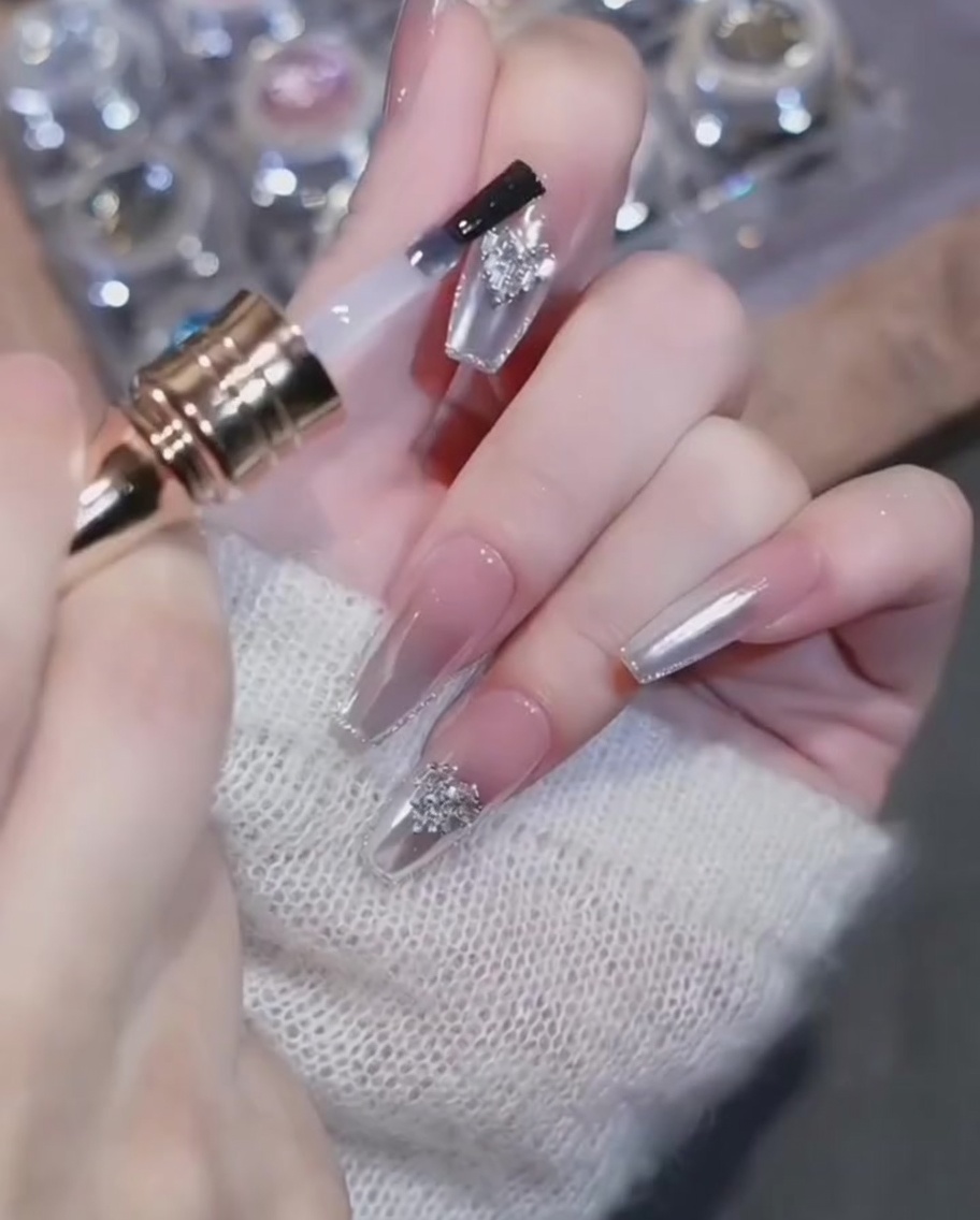 Un pennello da top coat che applica con cura il gel attorno a un ciondolo a cuore su ununghia cromata completata.