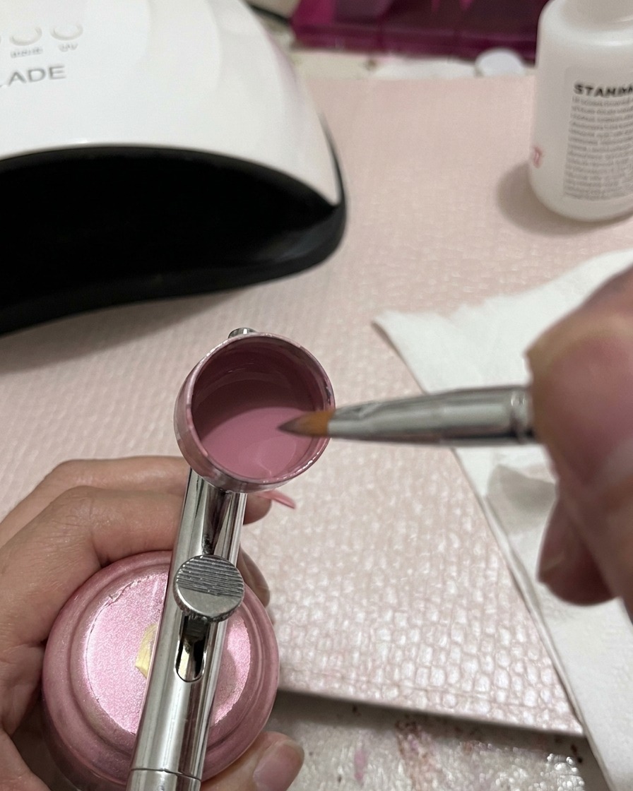 Dettaglio di uno strumento di miscelazione in metallo che mescola il gel rosa allinterno del serbatoio dellaerografo.
