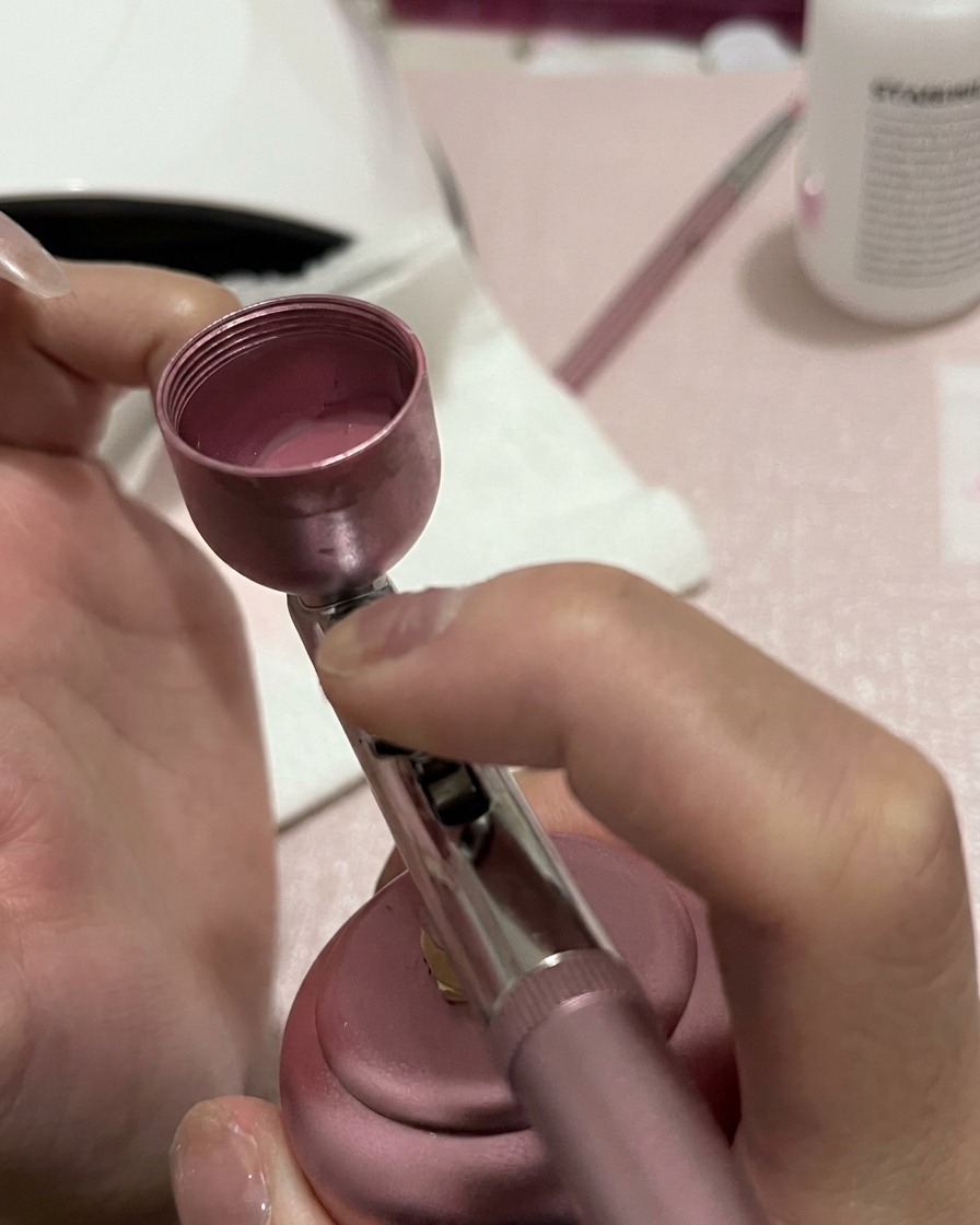 Primo piano di ununghia che riceve uno spruzzo più concentrato di pigmento rosa alla base e nella parte centrale.