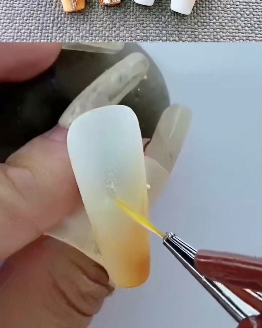 Pinzette posizionano un piccolo emblema metallico dorato sulla superficie del gel non ancora polimerizzato.