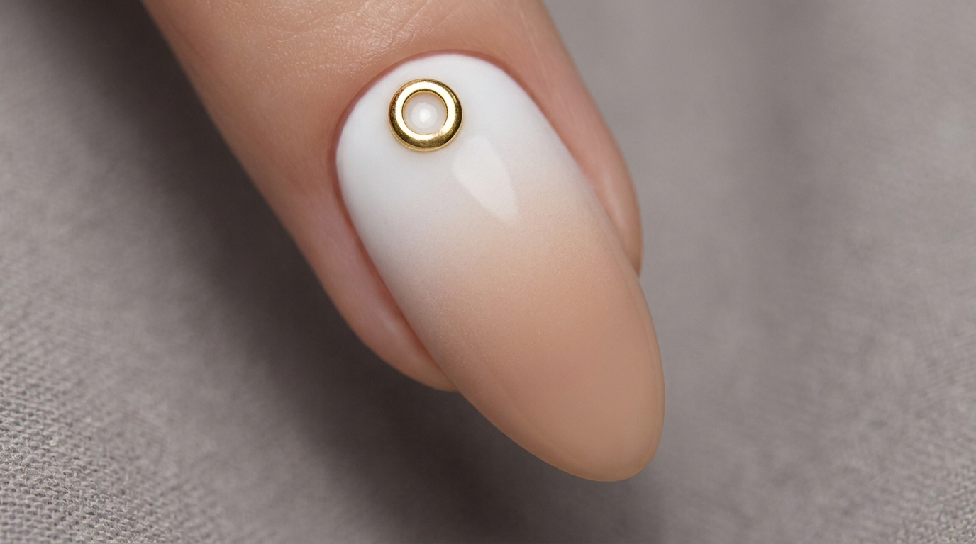 Una raffinata sfumatura unghie bianco-nude realizzata ad aerografo e impreziosita da un piccolo anello metallico minimalista.