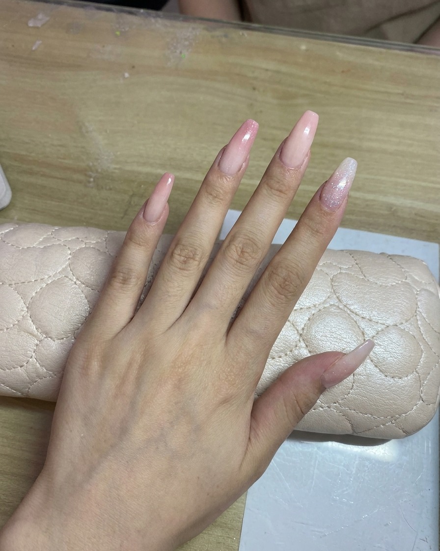 Una mano con unghie lunghe dai toni chiari durante lapplicazione di una delicata sfumatura rosa con aerografo.