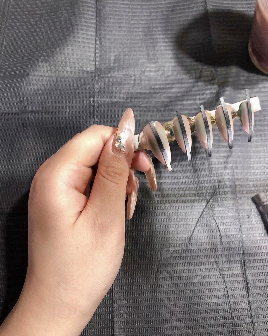 Una pistola per airbrush che spruzza uno strato sottile di gel bianco su unghie artificiali montate su un supporto.