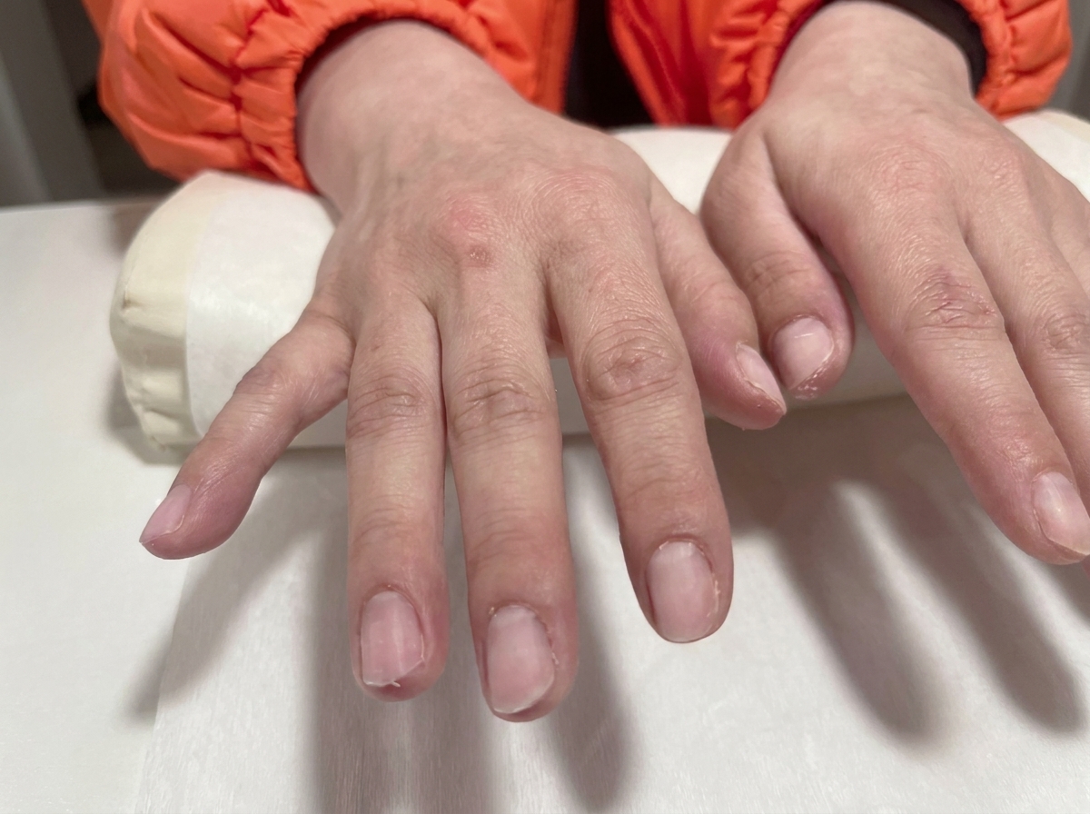 Primo piano di due mani con unghie in gel trasparente pronte su un cuscino da salone bianco.
