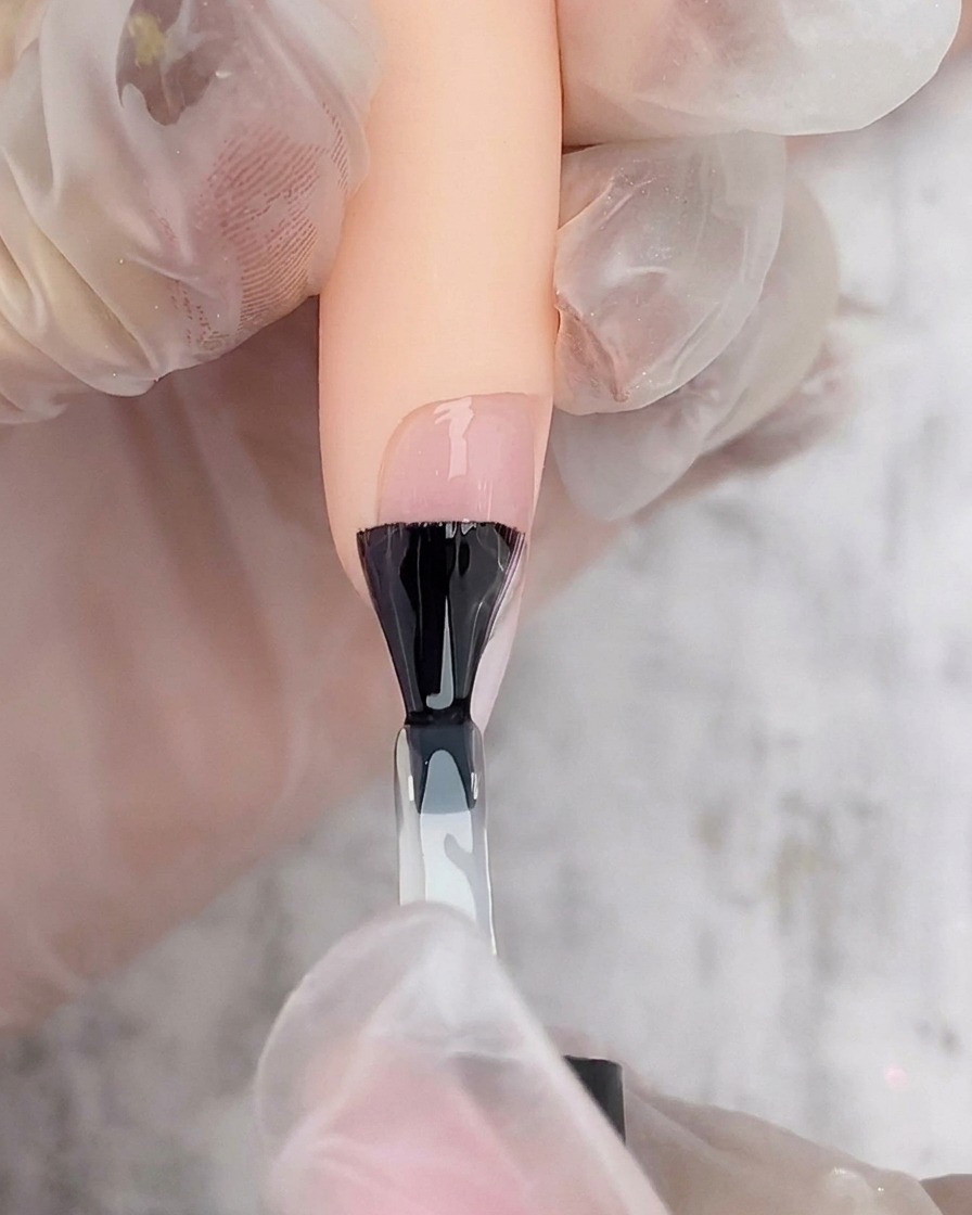 Un pennello nero che applica il top coat trasparente su ununghia ombré.