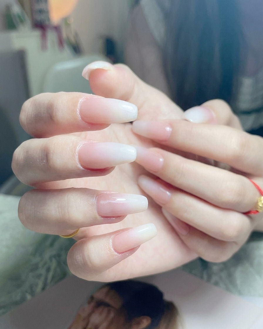 Pennello che applica uno strato finale di top coat trasparente su ununghia con ombré bianco finito.