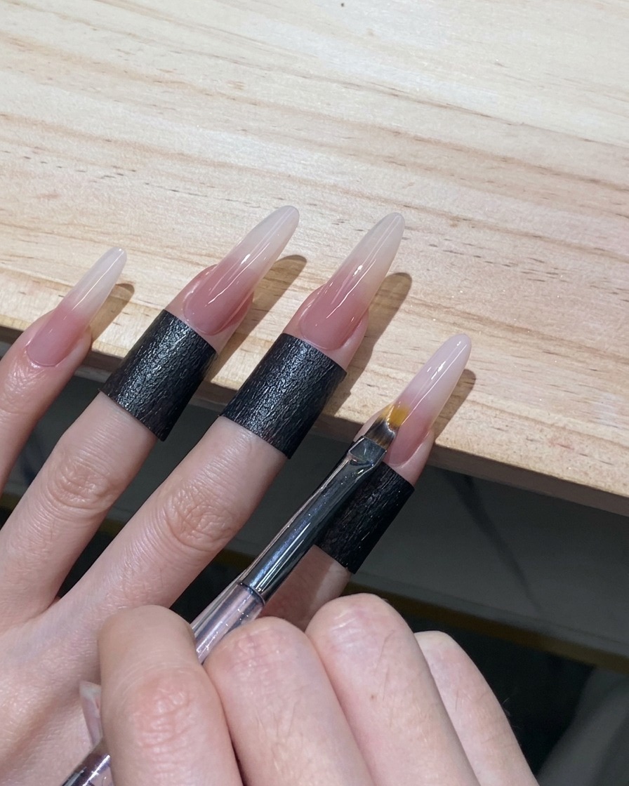 Un pennello da ombré utilizzato con leggeri movimenti di sfioramento per diffondere i margini del gel bianco su ununghia stiletto.