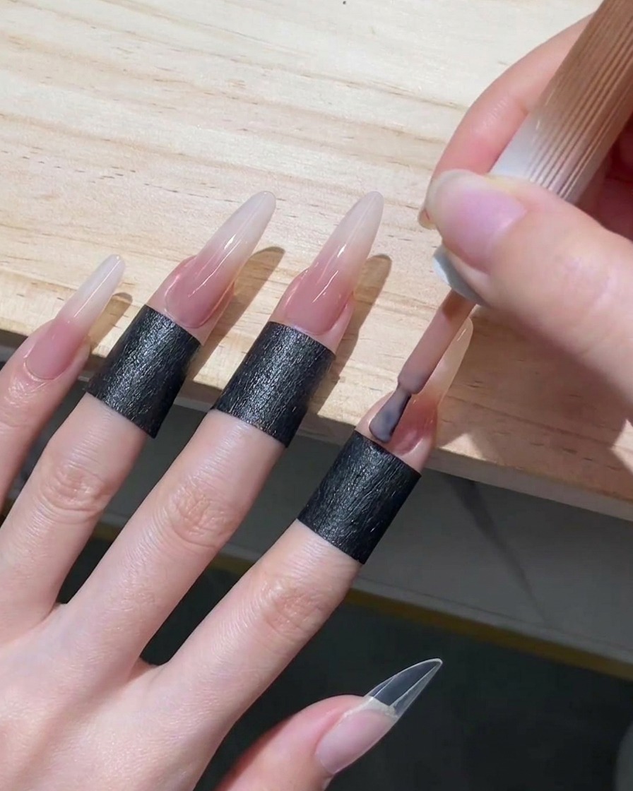 Applicazione di uno smalto gel nude rosato traslucido sulla zona delle cuticole e sulla metà inferiore di una lunga unghia stiletto.
