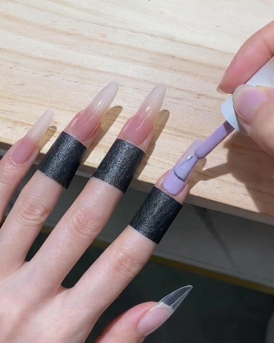 Un pennello per smalto gel che riempie la metà inferiore di ununghia stiletto con gel nude traslucido, spingendolo verso lalto fino a incontrare il bordo bianco diffuso.