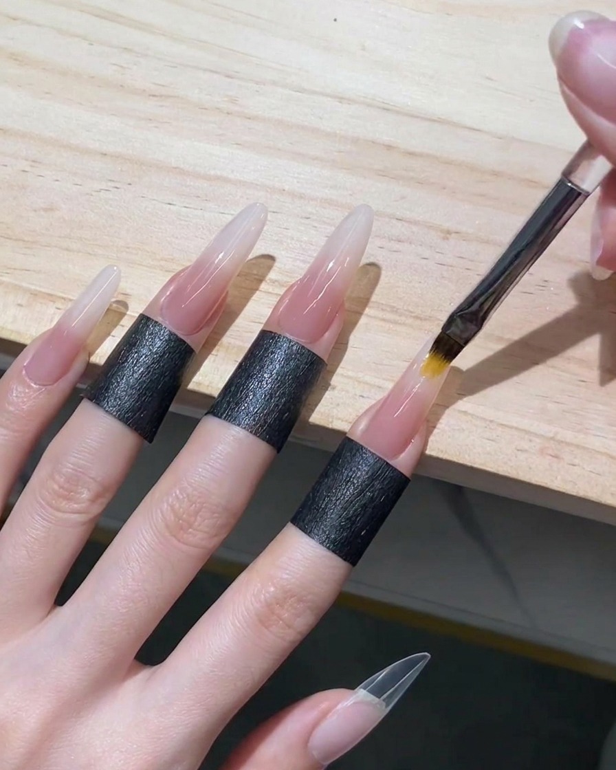 Un pennello da ombré che sfuma il gel nude traslucido verso lalto nel gel bianco bagnato su ununghia stiletto per creare una sfumatura senza interruzioni.