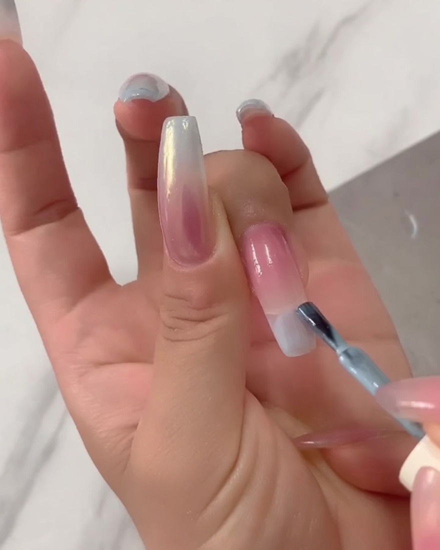Primo piano di un pennello che applica smalto gel azzurro puro direttamente sulla punta di una lunga estensione per unghie.