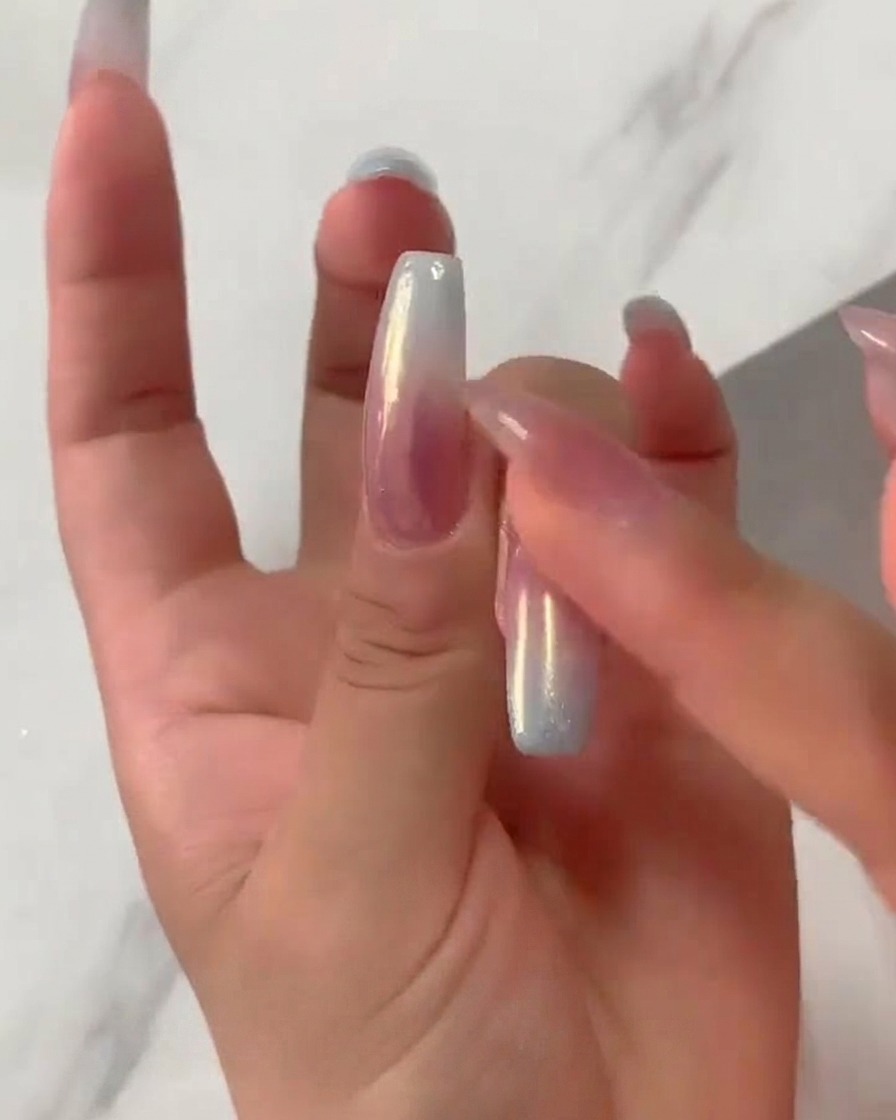Un polpastrello sfrega con fermezza la polvere iridescente aurora chrome su ununghia sfumata rosa e blu polimerizzata.