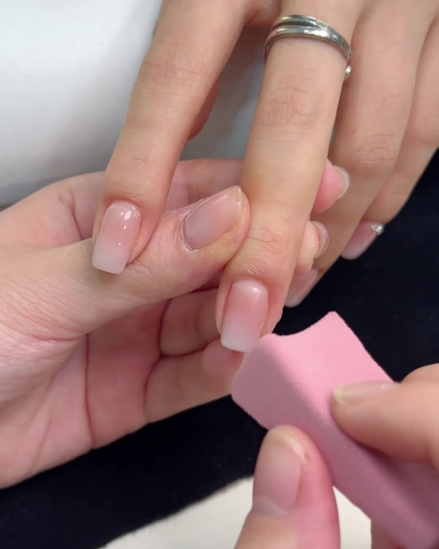 Una piccola spugnetta rosa che picchietta gel bianco sulla punta di ununghia per creare un effetto ombre.