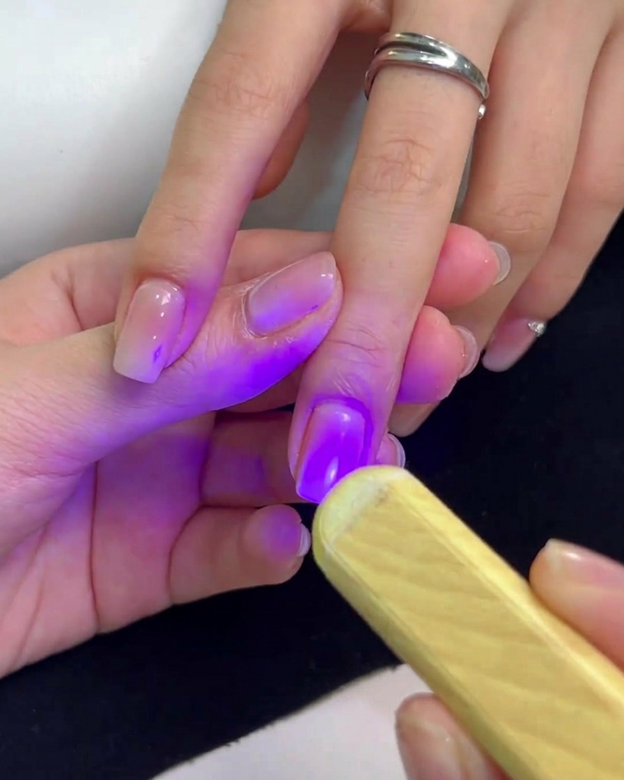 Una mini lampada UV portatile che emette luce viola tenuta sopra ununghia per polimerizzare lo smalto gel.