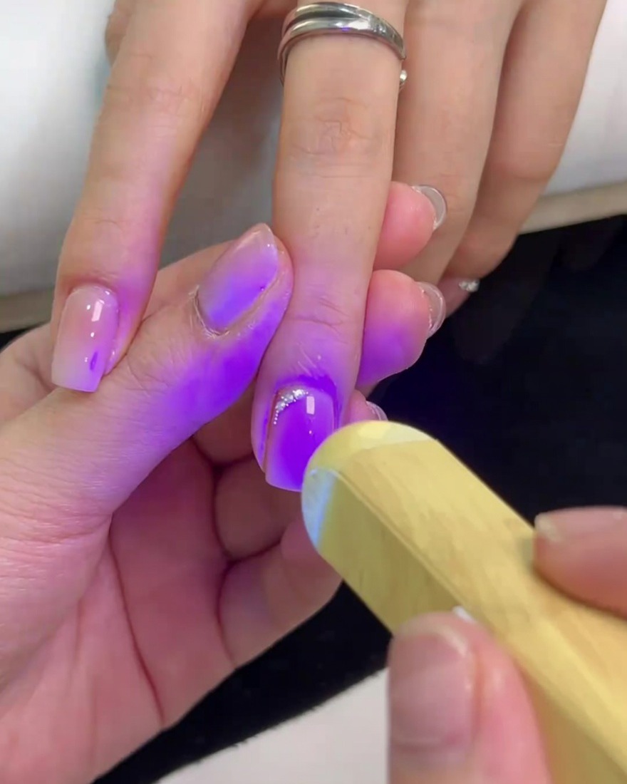 Una mini lampada UV portatile che illumina con luce viola ununghia quadrata per polimerizzare la colla degli strass e fissare i cristalli.