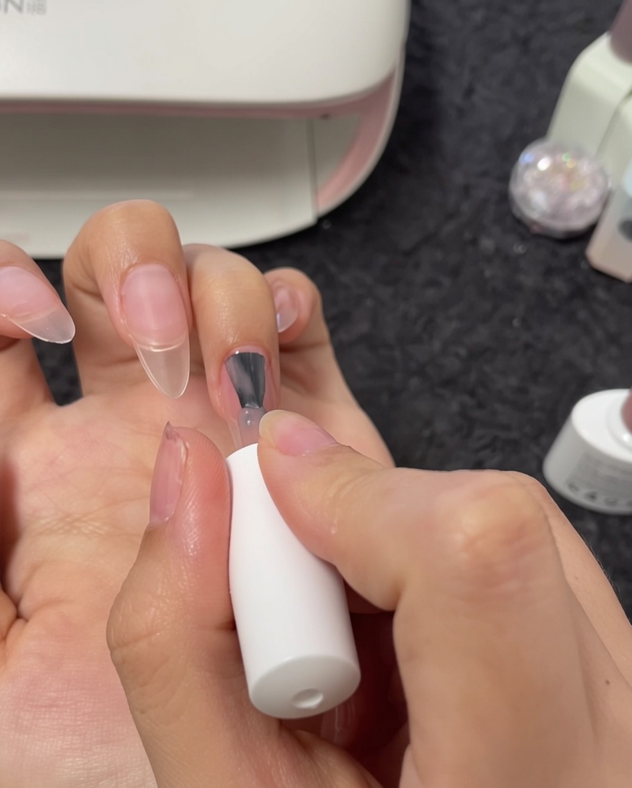 Primo piano di un pennello che applica lo smalto gel nude sullunghia del dito medio.