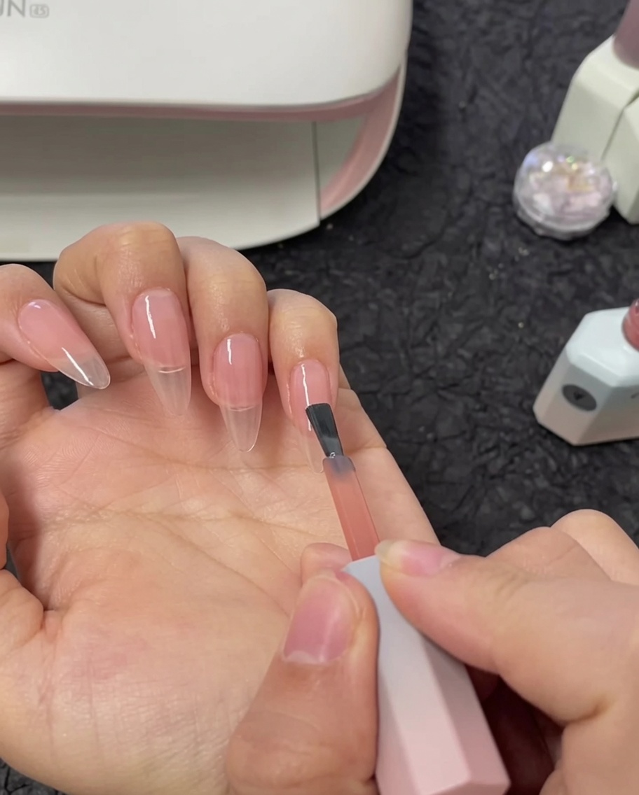 Un pennello che applica un secondo strato di smalto gel nude sullunghia dellindice.