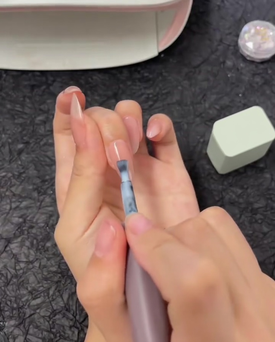 Un pennello che stende una striscia orizzontale di smalto gel bianco sulla metà superiore di ununghia.