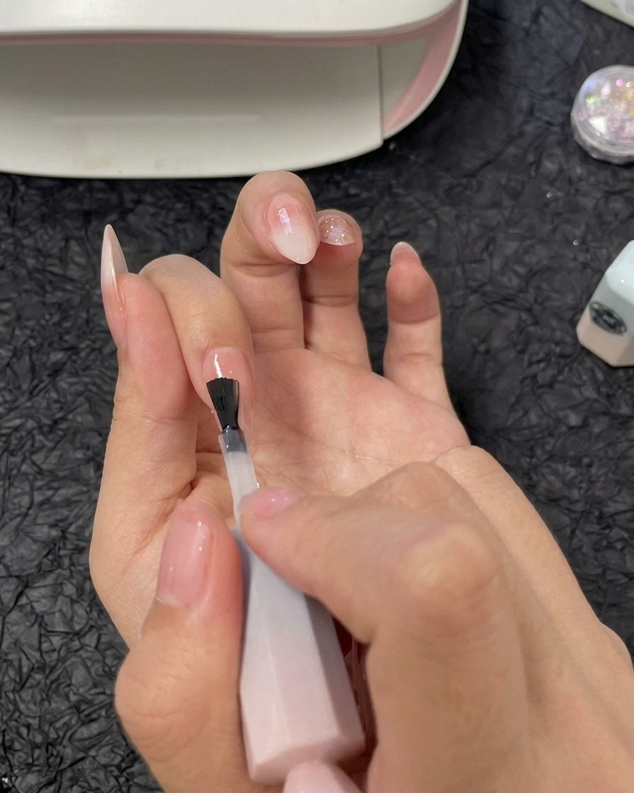Una mano che applica uno strato di gel costruttore trasparente sullunghia dellanulare utilizzando un pennello per smalto gel.