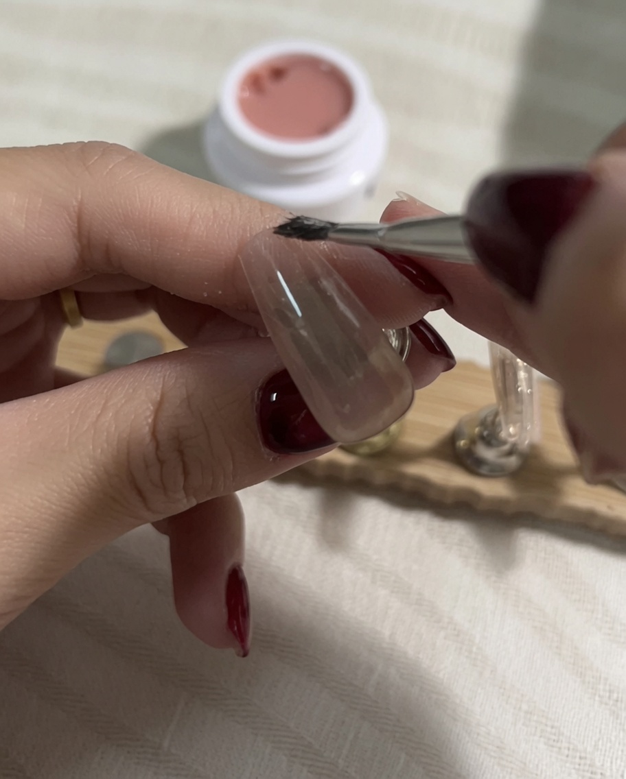 Prelevare una tonalità più chiara di smalto gel nude su un pennello piatto dopo che il precedente strato è stato polimerizzato.