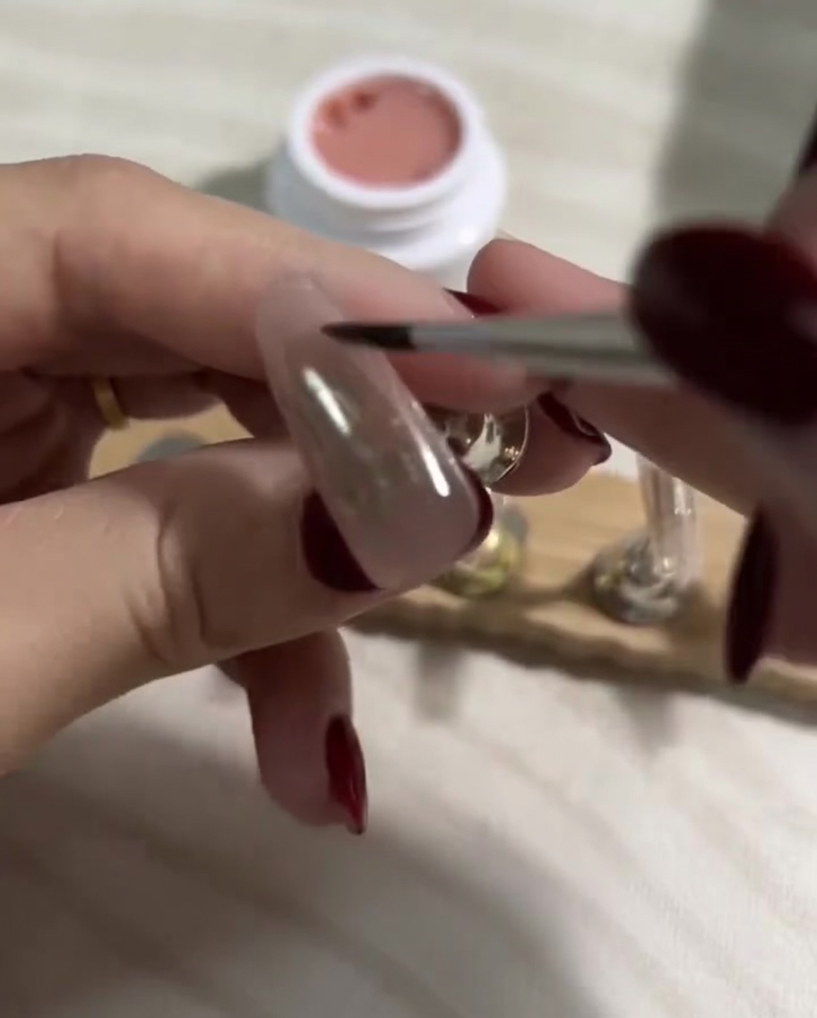 Pennellata di uno strato liscio di smalto gel nude chiaro sopra lo strato base scuro già polimerizzato su una press-on.