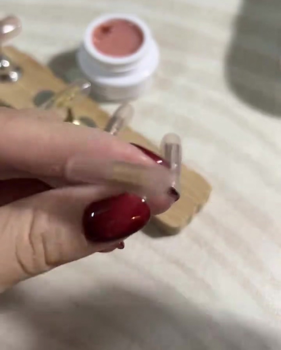 Un primo piano di una mano che usa una salvietta priva di lanugine imbevuta di cleaner per unghie per pulire la superficie delle press-on polimerizzate.