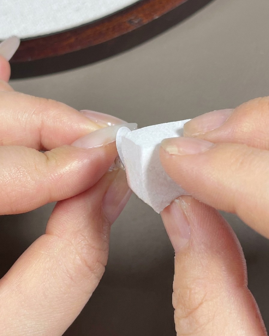 Una spugnetta da trucco che tampona del gel bianco sulla punta di una lunga unghia a mandorla.