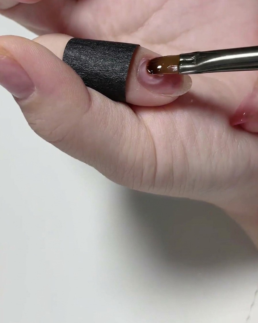 Un pennello di precisione applica un gel strutturale trasparente su ununghia naturale.