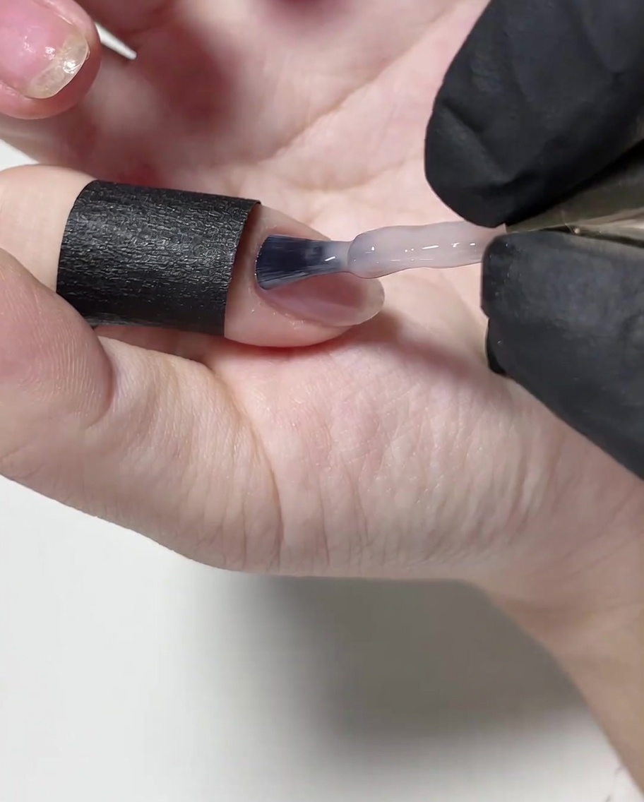 Un pennello applica uno strato sottile di smalto gel nude sulla superficie dellunghia.