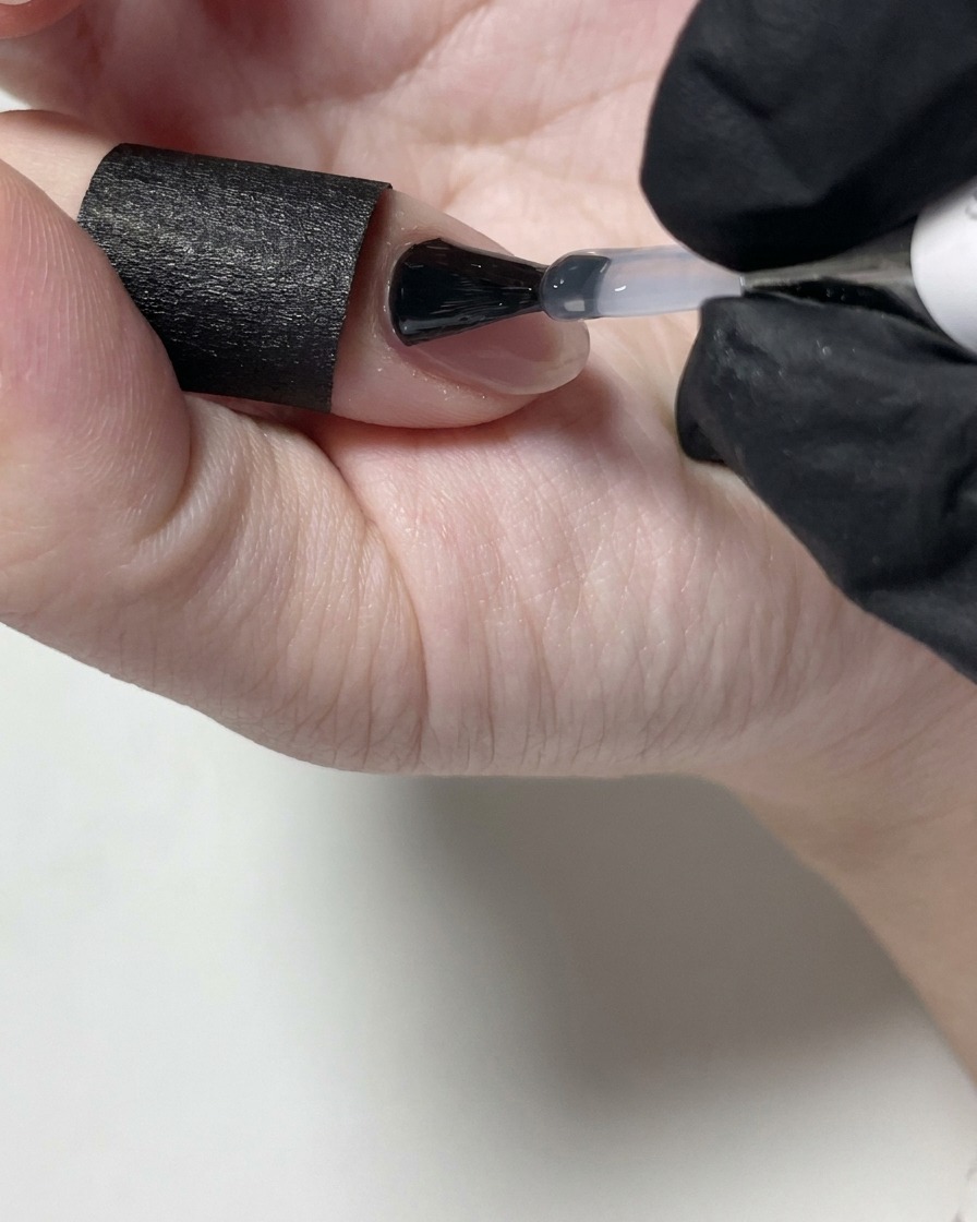 Unonicotecnica applica un top coat opaco trasparente sopra ununghia in gel nude usando un pennello nero.